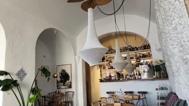A white vaulted space with hanging woven lamps, a bottle bar and greenery in the corner