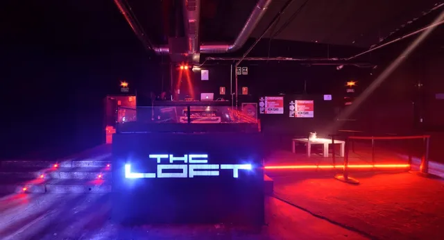 A DJ booth with an illuminated sign in a dark hall, in red and blue lights