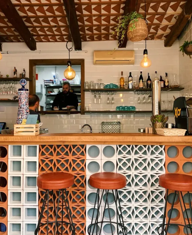 A wooden counter on patterned blocks with red stools and a kitchen window behind