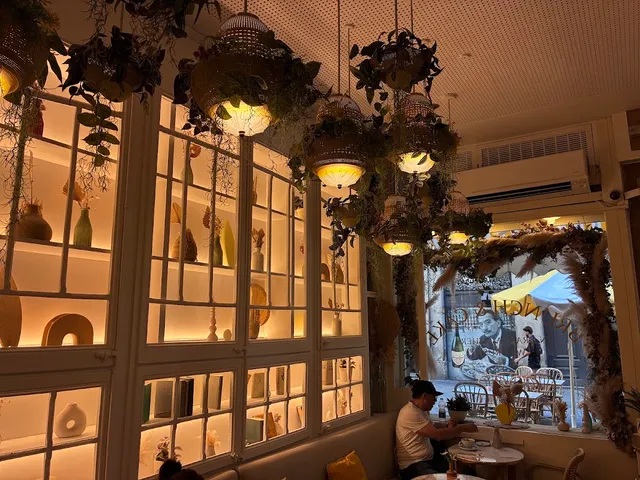 A room with lit white shelves, hanging plants and straw lamps above small tables