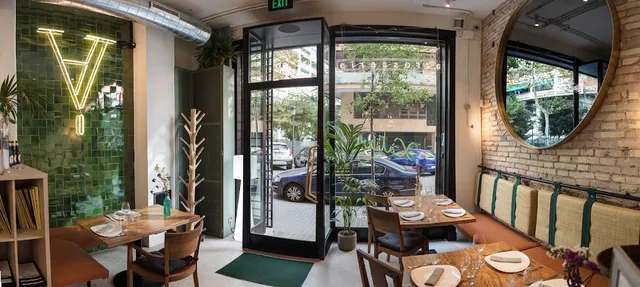 A dining room with a green tiled wall, a neon sign, a round mirror and a glass door to the street