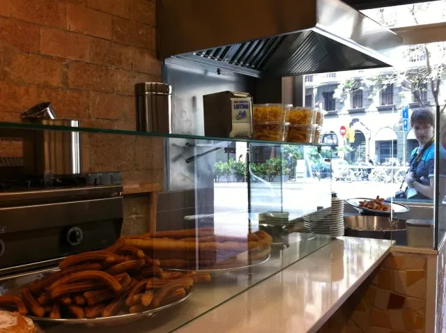 A pile of fried dough strips on a metal tray behind a glass display case