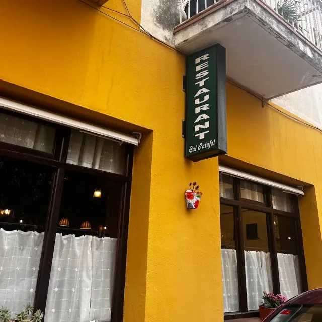 A bright yellow wall with a green vertical sign and windows with lace curtains
