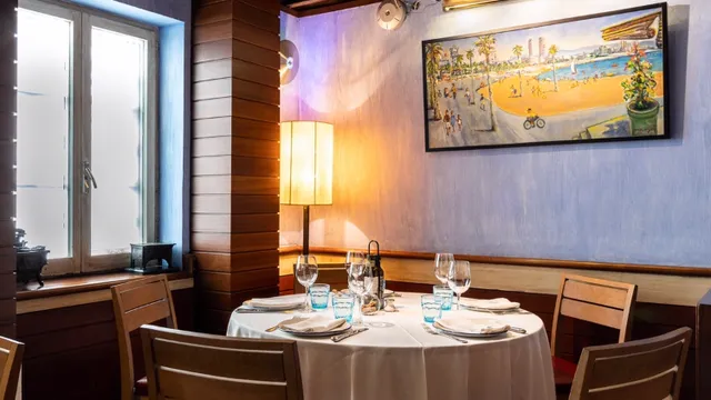A round table set in a white cloth beside a floor lamp, with a painting of a beach above it
