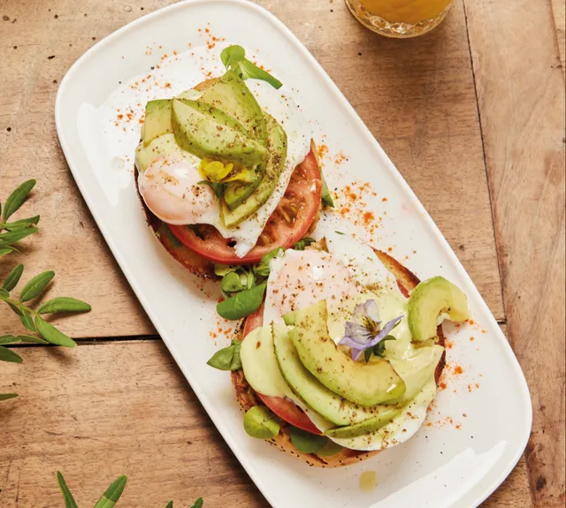 Poached eggs on avocado and tomato, on a long white plate on a wooden table