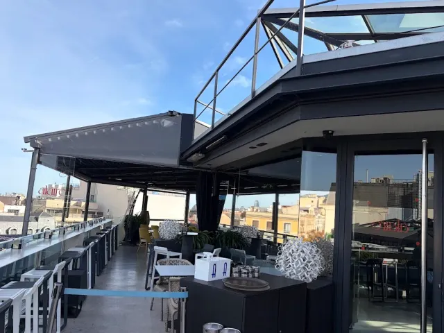 A rooftop terrace with a retractable awning, a glass railing and city roofs on the horizon
