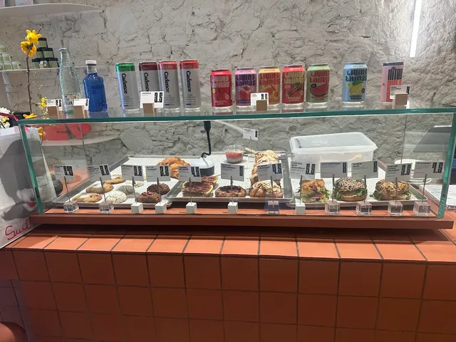 A glass display case with bagels and pastries below a row of colourful cans, on an orange tiled counter