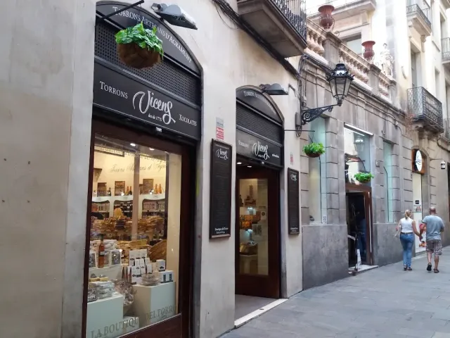 A narrow alley with a sweets shop window, an iron lamp and balconies above