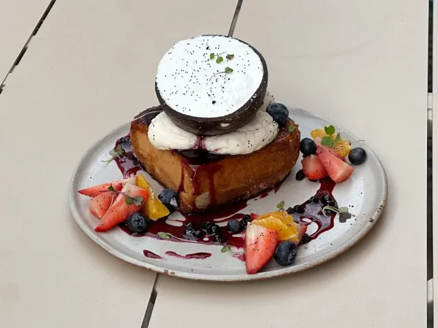 A fried slice of bread with cream, half a coconut and berries on a plate