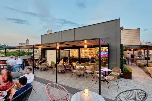 A roof terrace with people seated at dusk, and an old bell tower on the horizon