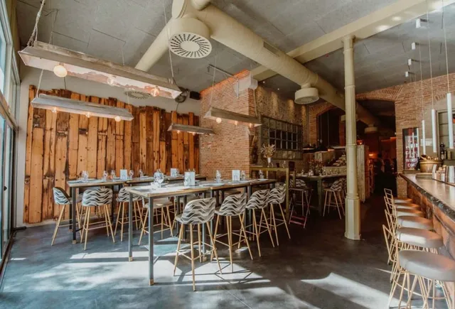 A bright room with high tables, zebra patterned stools, brick walls and a wooden wall