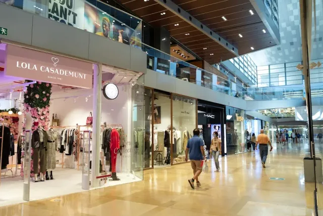A lit mall corridor with clothing shops on both sides and shoppers walking down the aisle