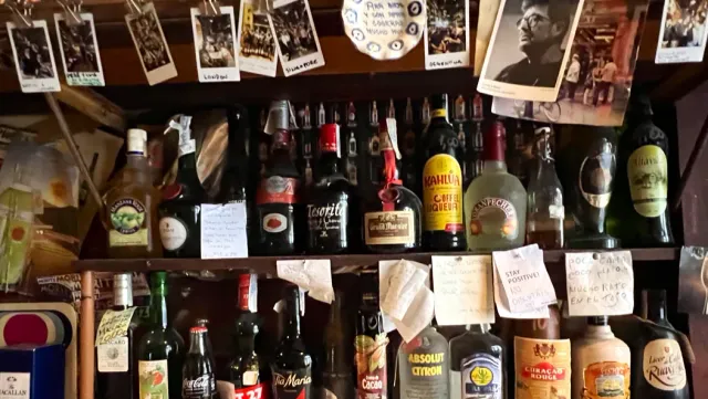 Crowded shelves of bottles with handwritten notes and old photographs hung above