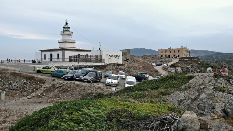 White lighthouse on a rocky cape with parked cars and low scrub